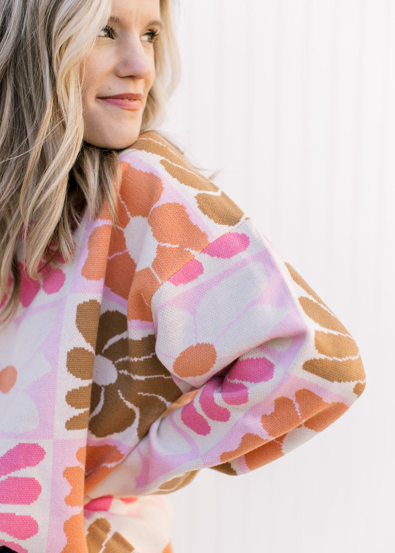 Close up of oversized orange, pink, rust and taupe flowers on a cream long sleeve sweater.