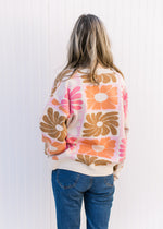 Back view of Model wearing a cream sweater with orange, pink, rust and taupe flowers.