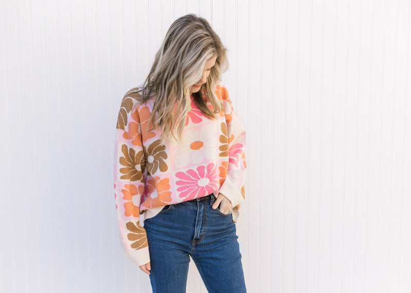 Model wearing jeans with a cream sweater with oversized orange, pink, rust and taupe flowers.