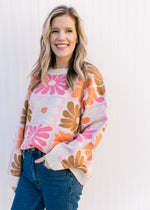 Model wearing jeans with a cream long sleeve sweater with orange, pink, rust and taupe flowers.