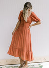 Model wearing a v-neck rust midi with bubble short sleeves and a smocked band in back. 