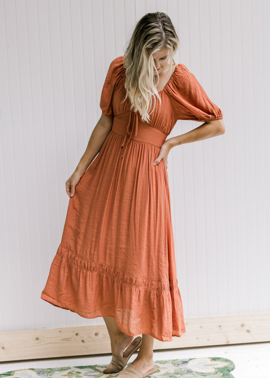 Model wearing a v-neck rust midi with bubble short sleeves and a smocked band in back. 