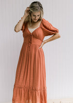Model wearing a rust midi with bubble short sleeves, v-neck with a tie and a ruffle at the hem. 