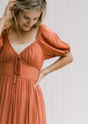 Close up of a v-neck with a tie and bubble short sleeve on a rust midi dress with a bottom ruffle. 