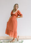 Model wearing sandals with a v-neck rust midi with bubble short sleeves and a smocked band in back. 
