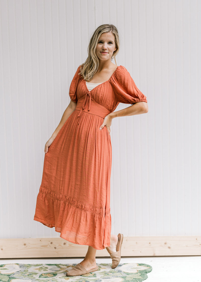 Model wearing sandals with a v-neck rust midi with bubble short sleeves and a smocked band in back. 