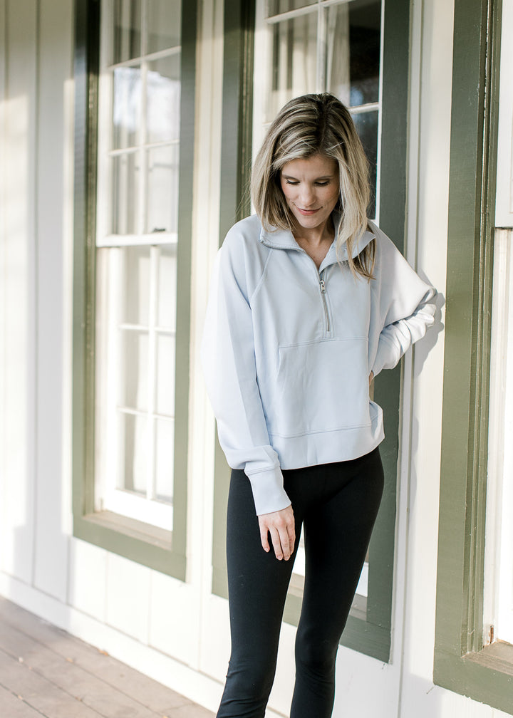 Model wearing a pale blue ribbed pullover with a quarter zip, front pouch pocket and long sleeves. 