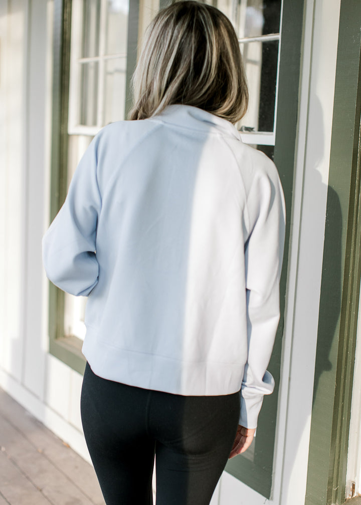 Back view of Model wearing a pale blue ribbed pullover with a front pouch pocket and long sleeves. 