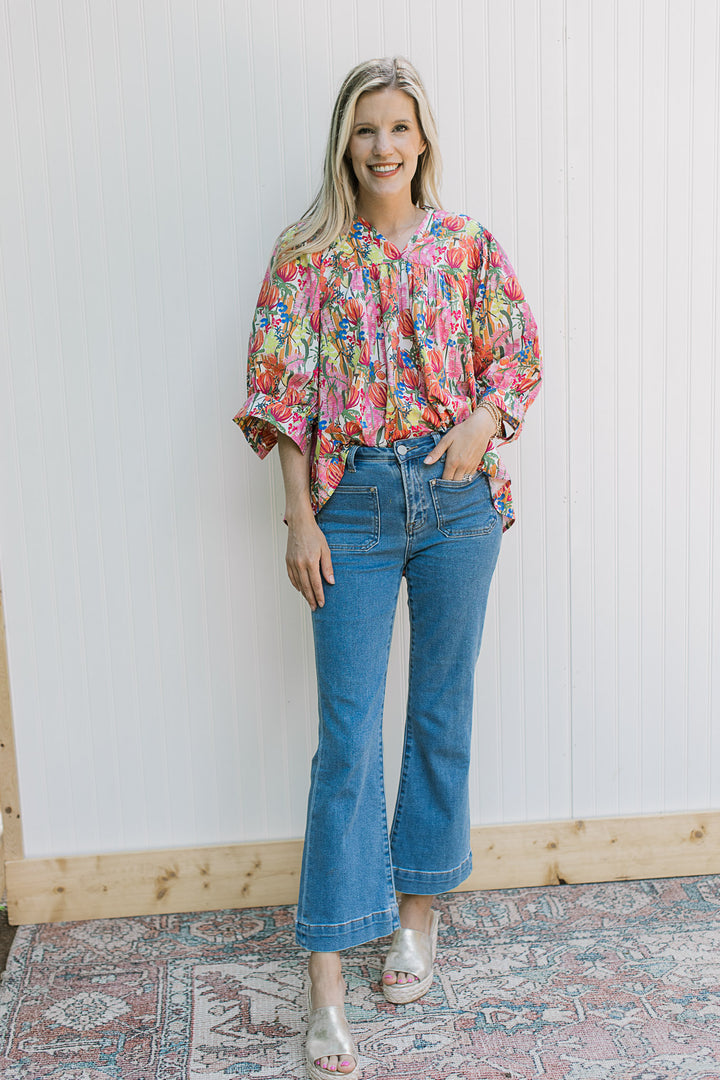Model wearing jeans and wedges with a white top with bright floral patter and 3/4 sleeve with cuff.