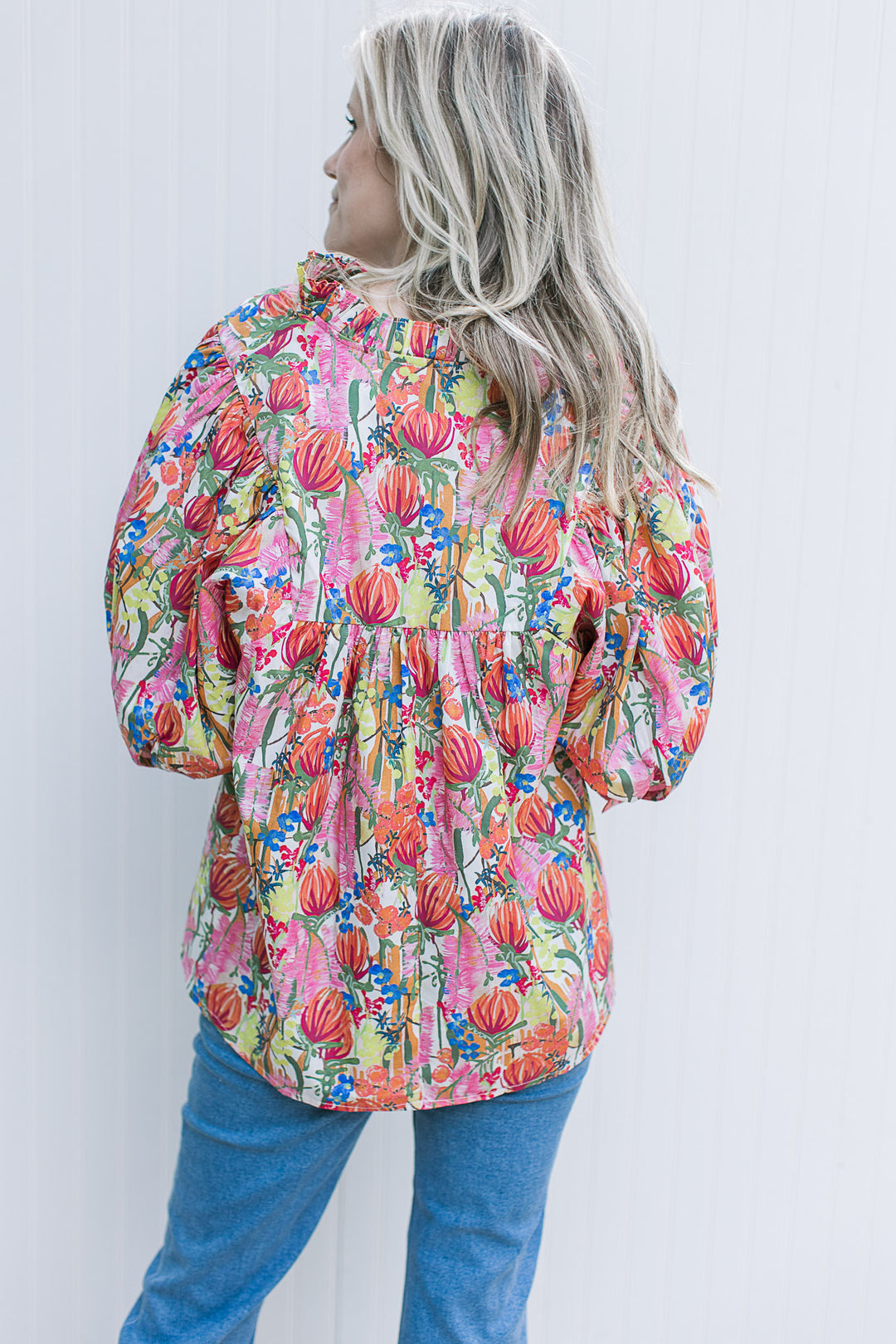 Back view of Model wearing a white top with bright floral patter, 3/4 sleeve with cuff and v-neck.