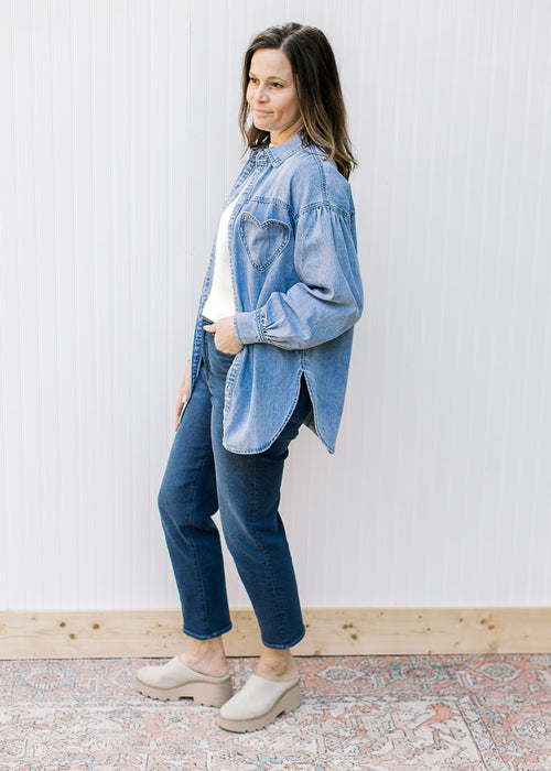 Model wearing an oversized chambray button down with long sleeves and a detail heart pocket. 