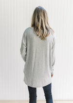 Back view of a Model wearing an oversized soft gray knit top with long sleeves and a round neck. 