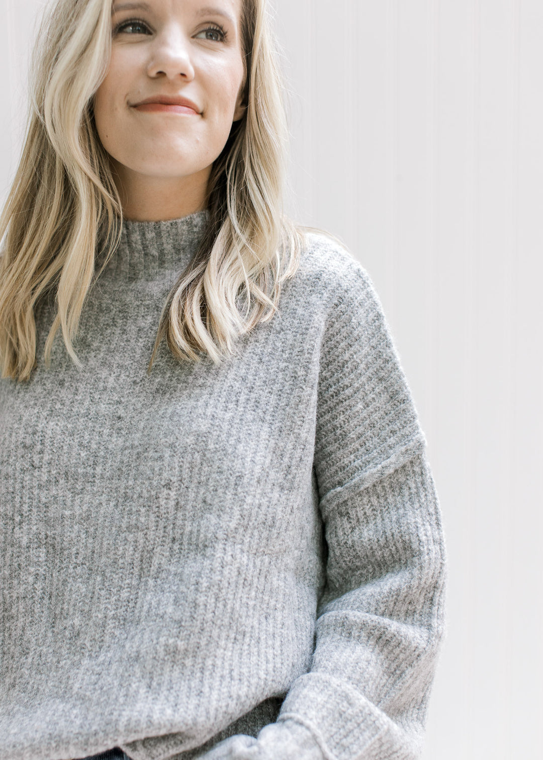 Close up of mock neckline and ribbing on a gray long sleeve sweater with split side hem. 