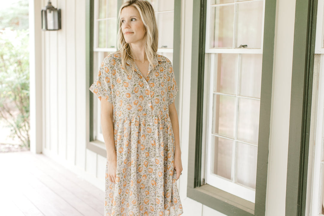 Model wearing a tan babydoll dress with orange flowers, short sleeves and a collar.