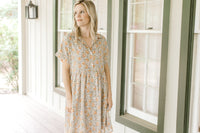 Model wearing a tan babydoll dress with orange flowers, short sleeves and a collar.