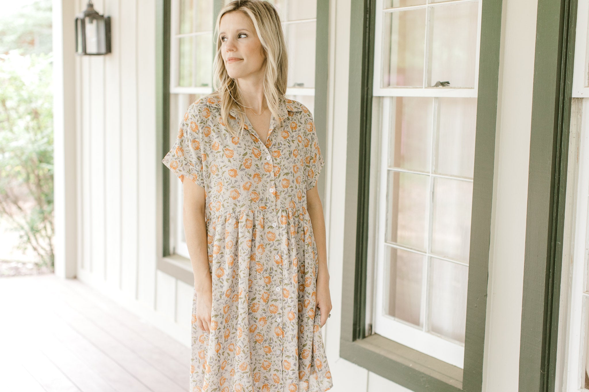 Model wearing a tan babydoll dress with orange flowers, short sleeves and a collar.