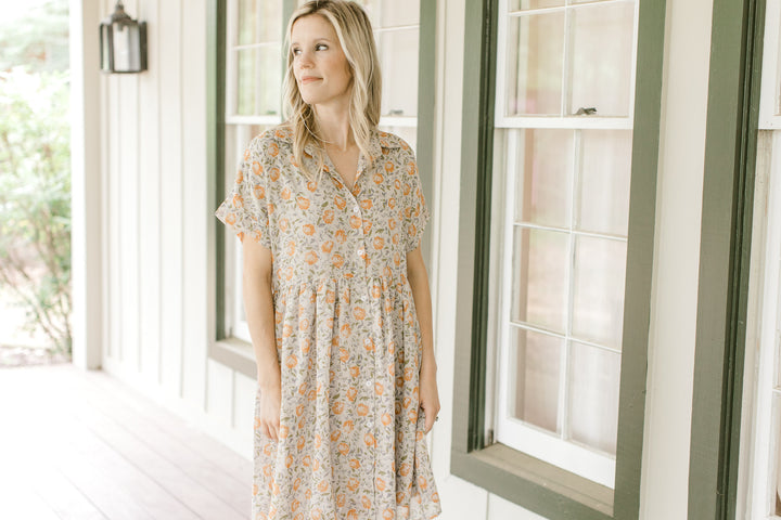 Model wearing a tan babydoll dress with orange flowers, short sleeves and a collar.