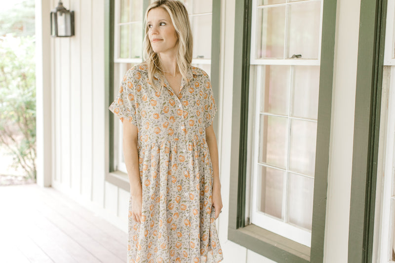 Model wearing a tan babydoll dress with orange flowers, short sleeves and a collar.