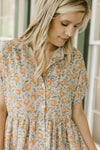 Close up of orange flowers on a tan dress with button front, short sleeves and a collar.