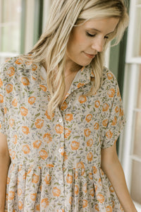 Close up of orange flowers on a tan dress with button front, short sleeves and a collar.