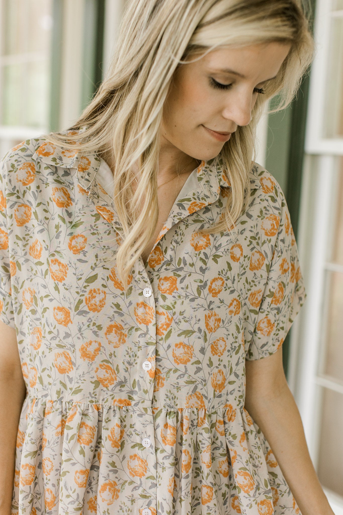 Close up of orange flowers on a tan dress with button front, short sleeves and a collar.