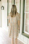 Back view of Model wearing a tan button up dress with orange flowers, short sleeves and a collar.