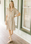 Model wearing sandals with a tan button up dress with orange flowers, short sleeves and a collar.