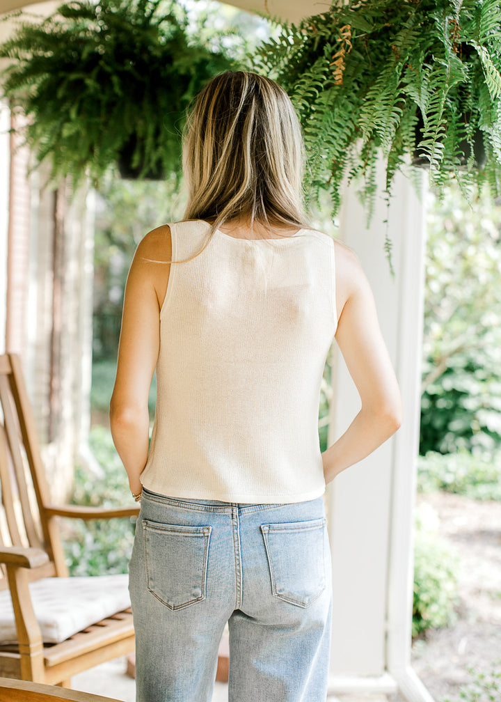 Back view of Model wearing a cream knit sweater with a sleeveless design and a v-neck. 