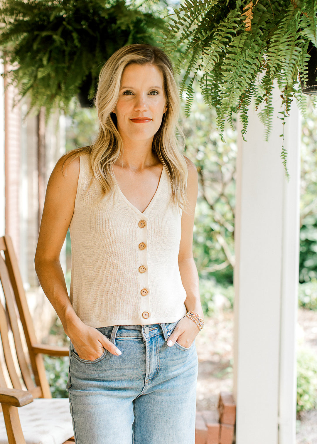 Model wearing a cream knit sweater with a sleeveless design, v-neck and button front. 