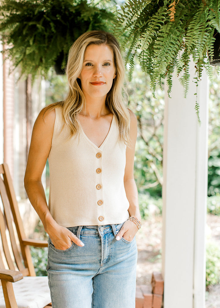Model wearing a cream knit sweater with a sleeveless design, v-neck and button front. 