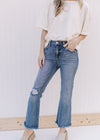 Model wearing a cream top with distressed medium wash flare jeans with a raw hemline.