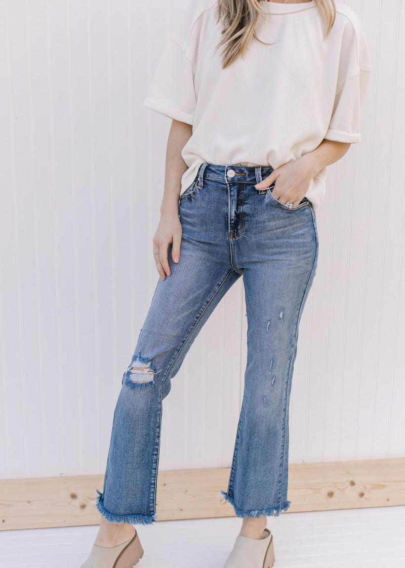 Model wearing a cream top with distressed medium wash flare jeans with a raw hemline.