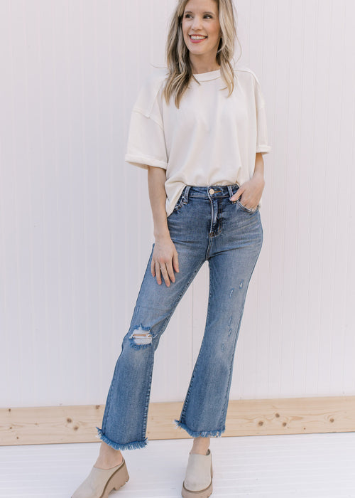 Model wearing distressed medium wash flare jeans with a raw hemline and button and zip closure.