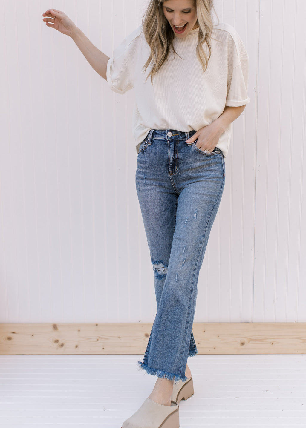 Model wearing distressed medium wash flare jeans with a cropped fit and raw hemline.