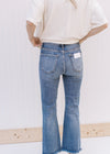 Back view of Model wearing distressed medium wash jeans with a raw hem and button and zip closure.