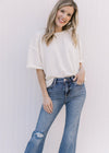 Model wearing distressed medium wash flare jeans with a raw hem and button and zip closure.