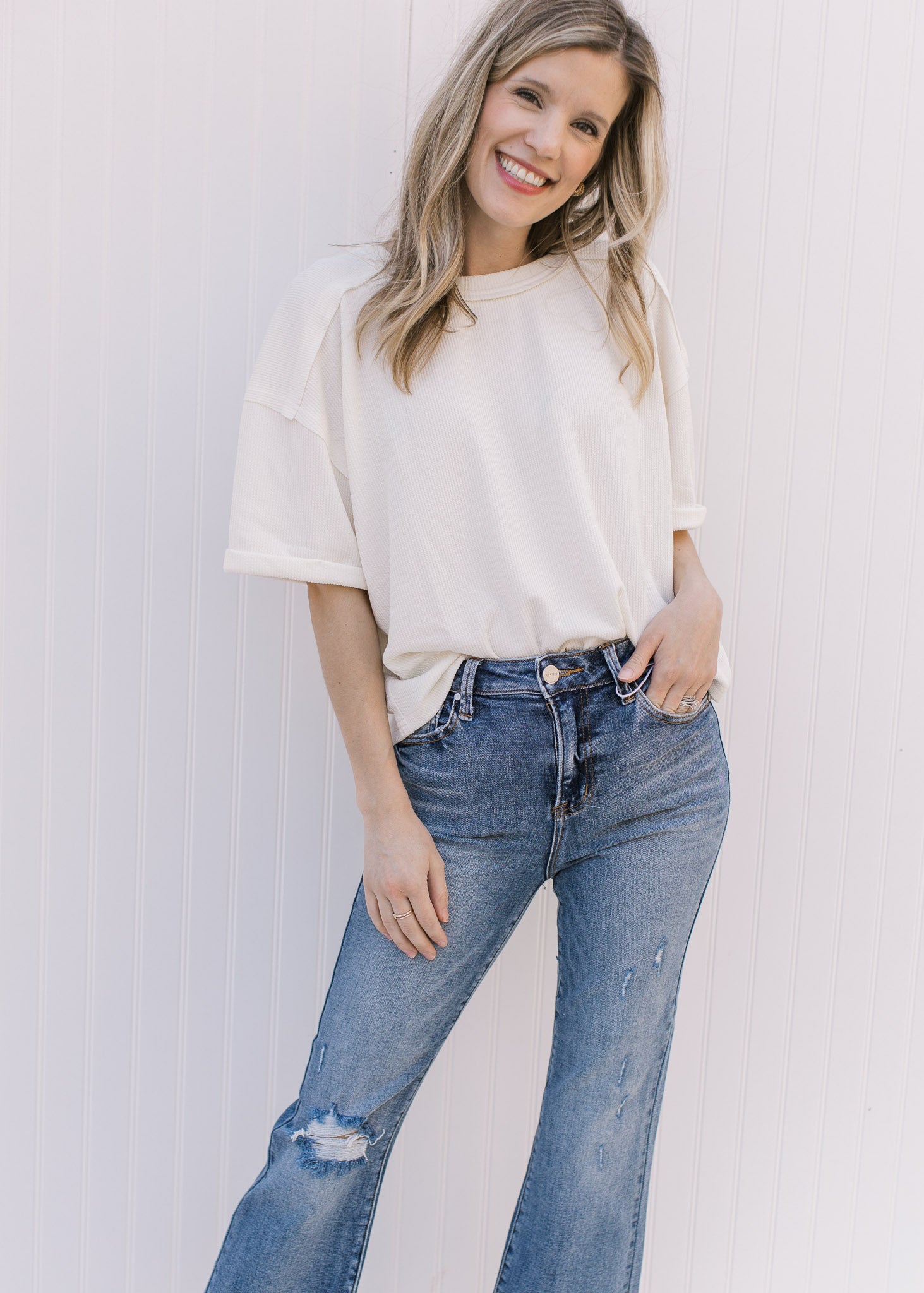 Model wearing distressed medium wash flare jeans with a raw hem and button and zip closure.