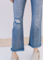 Close up of distressing and raw hemline on medium wash cropped jeans. 