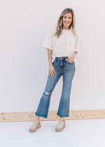 Model wearing mules, a cream top and distressed medium wash flare jeans with a raw hemline.