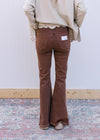 Back view of Model wearing espresso colored  jeans with side splits, raw hem and a flare leg. 