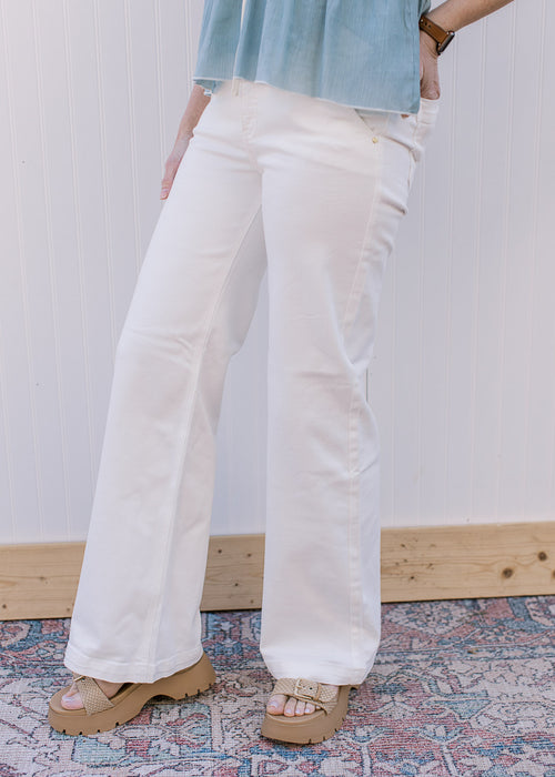 Model wearing sandals and white, wide leg pants with a high rise fit, stretch and side slit pockets.