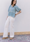 Model wearing a blue top and white, wide leg pants with a high rise fit and side slit pockets.