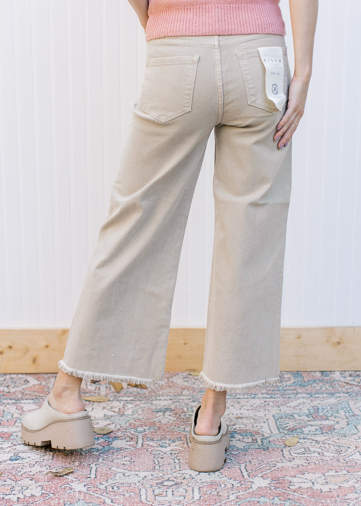 Back view of Model wearing khaki high rise jeans with a cropped fit, frayed hem and wide legs. 