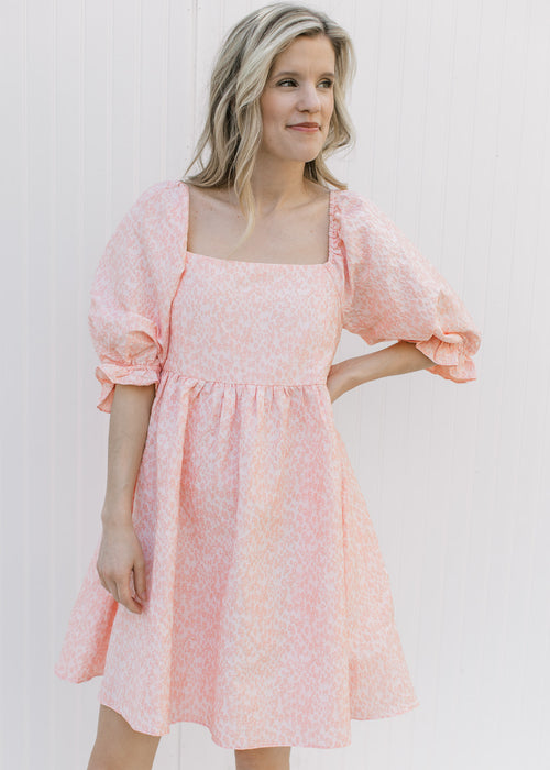 Model wearing a pink dress with textured microfloral pattern, square neck and 3/4 poet sleeves.