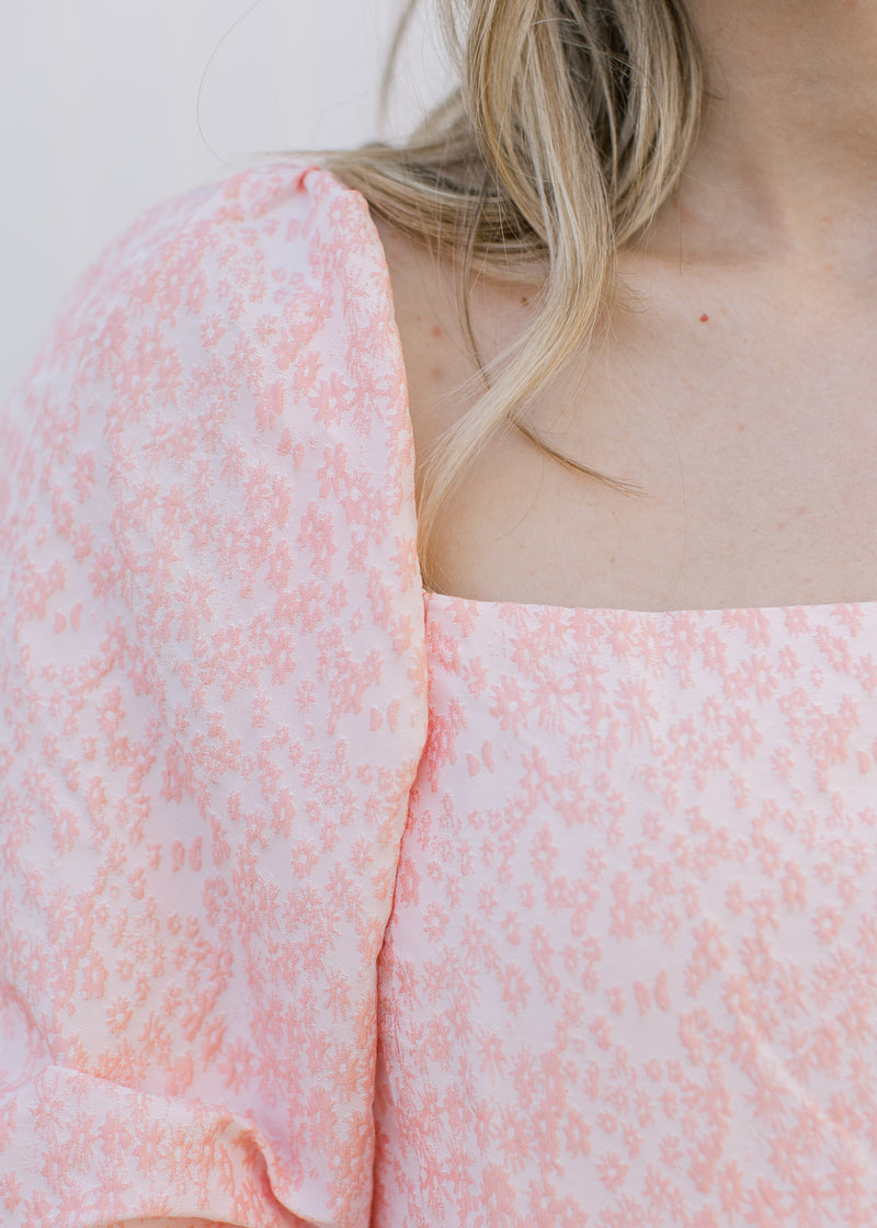 Close up of square neckline and pink textured microfloral on a soft pink background.