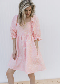 Model wearing a pink above the knee dress with a soft pink textured microfloral and a square neck.