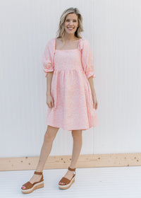 Model wearing heels and a pink dress with a soft pink microfloral pattern and a square neck.