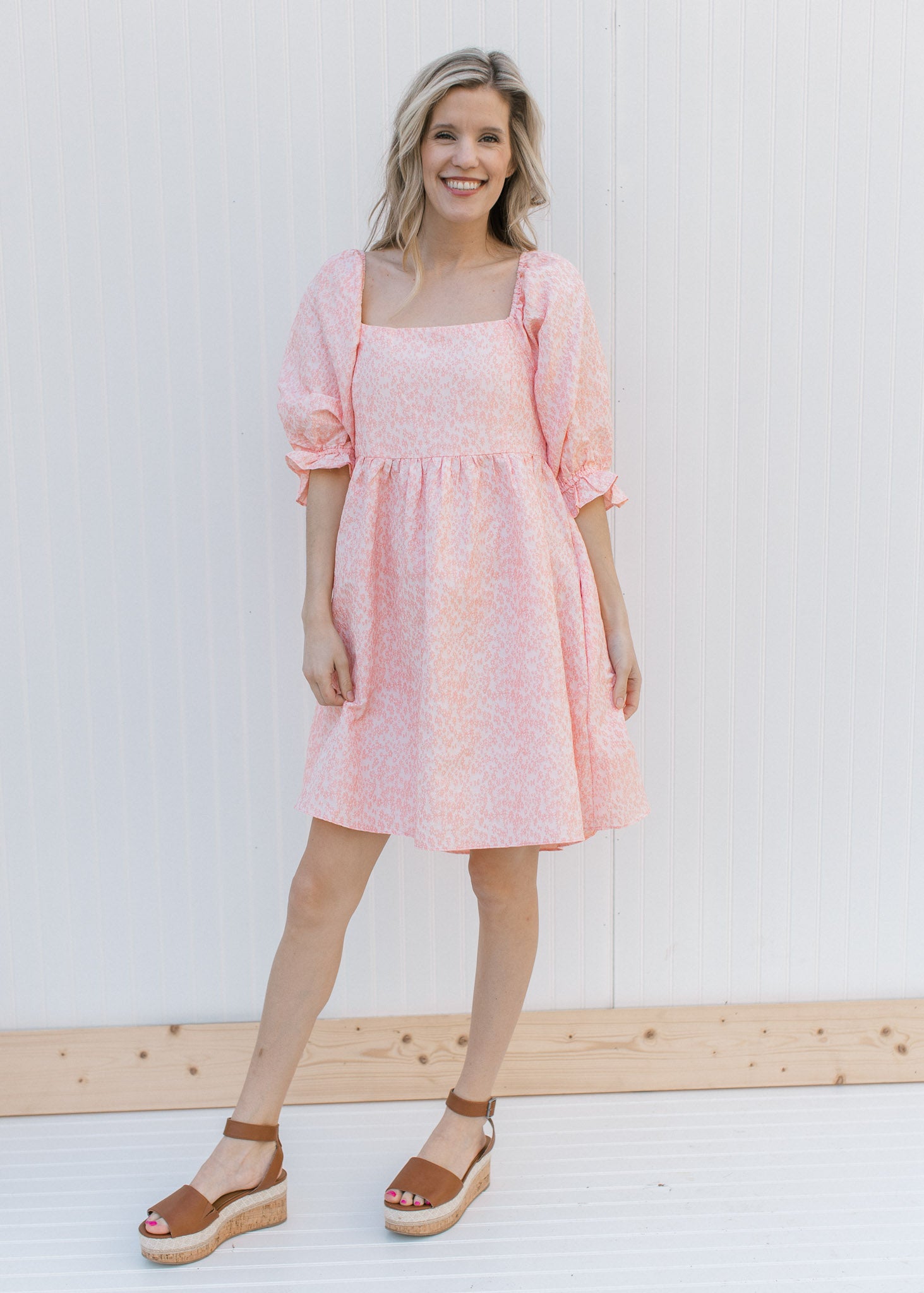Model wearing heels and a pink dress with a soft pink microfloral pattern and a square neck.