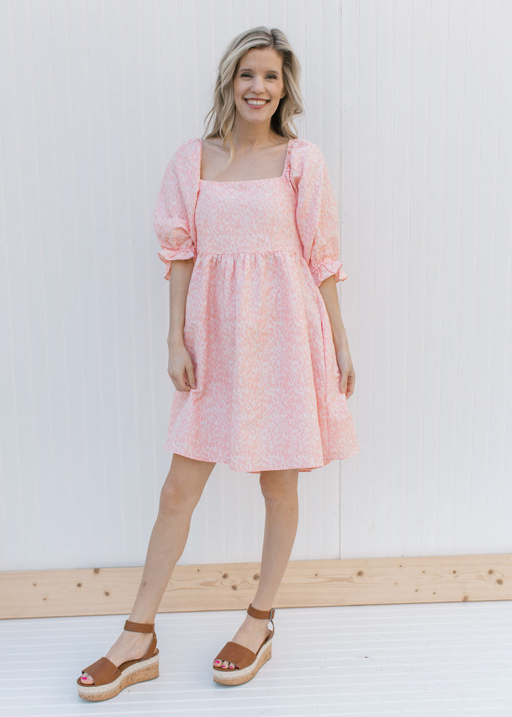 Model wearing heels and a pink dress with a soft pink microfloral pattern and a square neck.