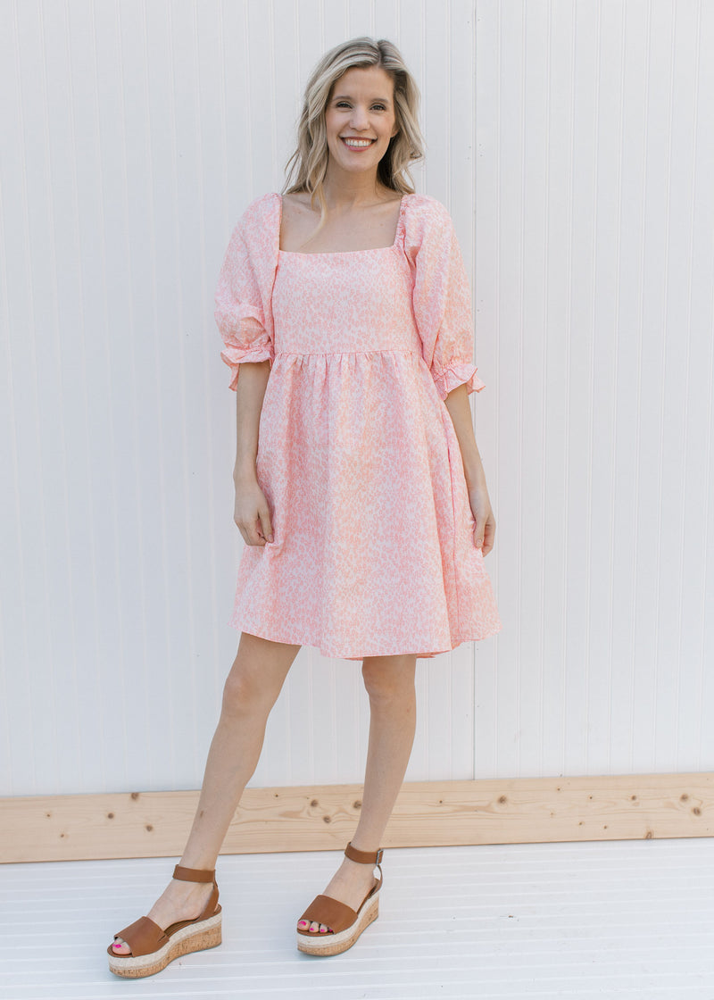 Model wearing heels and a pink dress with a soft pink microfloral pattern and a square neck.